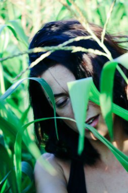 Yazın mısır yaprakları içinde güzel esmer bir kız, doğadaki bir kadının sanat portresi. Kameraya bakarak kahkahalar atmak, seçici keskinlik, açık iş gölgesi doğal ışık.