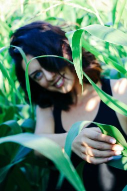 Yazın mısır yaprakları içinde güzel esmer bir kız, doğadaki bir kadının sanat portresi. Kameraya bakarak kahkahalar atmak, seçici keskinlik, açık iş gölgesi doğal ışık.
