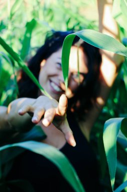 Yazın mısır yaprakları içinde güzel esmer bir kız, doğadaki bir kadının sanat portresi. Kameraya bakarak kahkahalar atmak, seçici keskinlik, açık iş gölgesi doğal ışık.