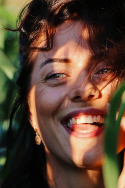 Yazın mısır yaprakları içinde güzel esmer bir kız, doğadaki bir kadının sanat portresi. Kameraya bakarak kahkahalar atmak, seçici keskinlik, açık iş gölgesi doğal ışık.