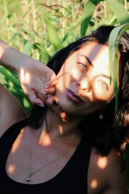 Yazın mısır yaprakları içinde güzel esmer bir kız, doğadaki bir kadının sanat portresi. Kameraya bakarak kahkahalar atmak, seçici keskinlik, açık iş gölgesi doğal ışık.