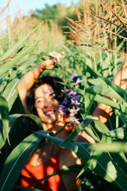 Yazın mısır yaprakları içinde güzel esmer bir kız, doğadaki bir kadının sanat portresi. Kameraya bakarak kahkahalar atmak, seçici keskinlik, açık iş gölgesi doğal ışık.