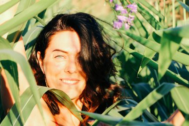 Yazın mısır yaprakları içinde güzel esmer bir kız, doğadaki bir kadının sanat portresi. Kameraya bakarak kahkahalar atmak, seçici keskinlik, açık iş gölgesi doğal ışık.