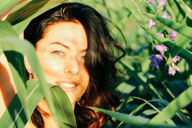 Yazın mısır yaprakları içinde güzel esmer bir kız, doğadaki bir kadının sanat portresi. Kameraya bakarak kahkahalar atmak, seçici keskinlik, açık iş gölgesi doğal ışık.