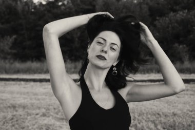Güneşli bir yaz akşamında poz veren genç ve güzel bir esmer. Çekici kadın farklı hareketler ifade eder, yakın plan portre, doğal açık siyah beyaz fotoğraf.