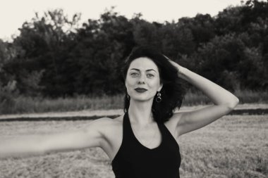 Güneşli bir yaz akşamında poz veren genç ve güzel bir esmer. Çekici kadın farklı hareketler ifade eder, yakın plan portre, doğal açık siyah beyaz fotoğraf.