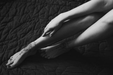 Ayaklarında kına dövmesi olan kadın bacaklarının ve ellerinin yakın çekimi. Siyah beyaz fotoğraf. Nazikçe kadınsı zarif dekorasyon, bir kadına saygı, sevgi ve kendine dikkat et..