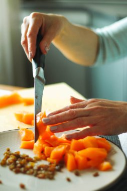 Yakın plan yetişkin kadın elleri turuncu balkabağını keser, mutfağında yemek hazırlar, sıradan bir ev hanımı. Doğal ışık, seçici keskinlik..