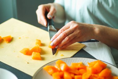 Yakın plan yetişkin kadın elleri turuncu balkabağını keser, mutfağında yemek hazırlar, sıradan bir ev hanımı. Doğal ışık, seçici keskinlik..