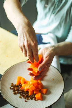 Yakın çekim kadın yetişkinler portakal kabağı ve kuru üzümlere dokunur, ev mutfağında yemek hazırlarlar, normal ev ışığı işlemleri, seçici keskinleştirme.