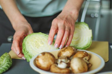 Yeşil lahana kesen kadın ellerinin yakın çekimi, ev mutfağında yemek hazırlamak, normal ev ışığı süreci, seçici keskinleştirme..