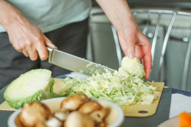 Yeşil lahana kesen kadın ellerinin yakın çekimi, ev mutfağında yemek hazırlamak, normal ev ışığı süreci, seçici keskinleştirme..