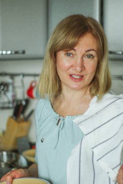 Evin mutfağında elinde cam kapakla gaz sobasının yanında duran ve mantar kızartan sarışın bir kadının dikiz görüntüsü. Doğal ışık basit bir evcil süreçtir.