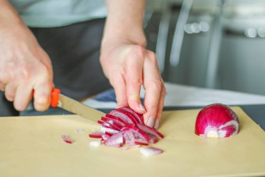 Kesme tahtasında kırmızı soğan kesen kadına yakın çekim, ev mutfağı aşçılığı, doğal ışık.