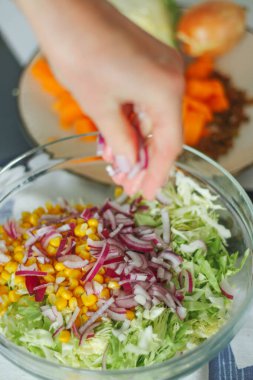 Sağlıklı yemek hazırlarken kadın elinin yakın plan çekimi, cam şeffaf tabakta salata, doğal ışık