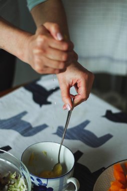 Sağlıklı yemek pişirirken kadın elinin yakın plan görüntüsü, limon suyunu bir kaba sıkıyor ve kaşıkla karıştırıyor, doğal ışık.