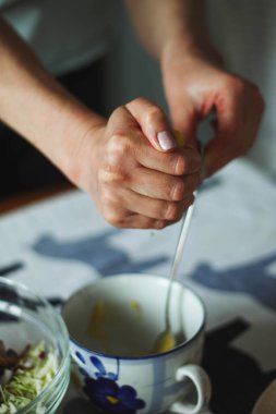 Sağlıklı yemek pişirirken kadın elinin yakın plan görüntüsü, limon suyunu bir kaba sıkıyor ve kaşıkla karıştırıyor, doğal ışık.