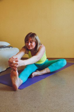 Yetişkin güzel Avrupalı kadın evde yoga yapıyor. Bir dizi yoga pozu. Pashchimottanasana bacakları bükerken sağlıklı yaşam tarzı konsepti, refah kişisel bakım