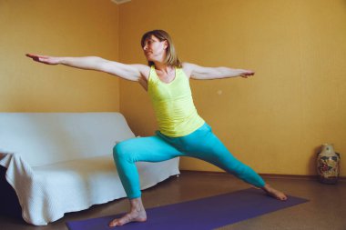 Yetişkin güzel Avrupalı kadın evde yoga yapıyor. Bir dizi yoga pozu. Virabhadrasana savaşçı duruşu. Sağlıklı yaşam tarzı konsepti, refah kişisel bakım
