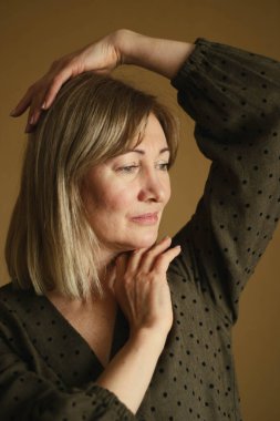 Doğal beyaz saçlı ve minimum makyajlı düşünceli olgun bir kadının sıradan portresi. Kahverengi, gevşek elbiseli.