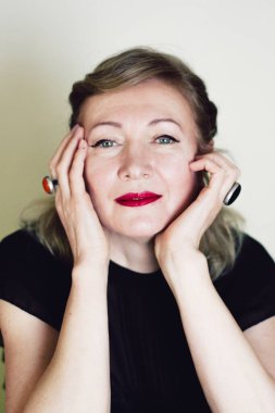 Zarif sarışın, orta yaşlı güzel bayan kameraya gülümsüyor. Retro makyaj ve saç stili, kırmızı dudaklar. Çekici bir kadın..