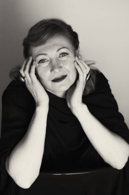 Zarif sarışın orta yaşlı güzel bayan kameraya gülümsüyor. Retro makyaj ve saç stili. Çekici bir kadın portresi. Dikey olarak siyah beyaz fotoğraf