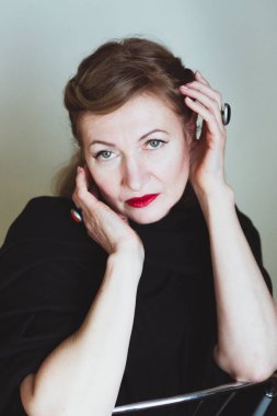 Zarif sarışın, orta yaşlı güzel bayan kameraya gülümsüyor. Retro makyaj ve saç stili, kırmızı dudaklar. Çekici bir kadın..