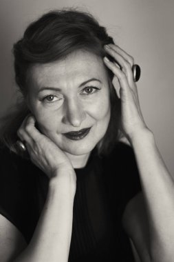 Zarif sarışın orta yaşlı güzel bayan kameraya gülümsüyor. Retro makyaj ve saç stili. Çekici bir kadın portresi. Dikey olarak siyah beyaz fotoğraf