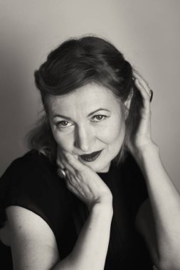 Zarif sarışın orta yaşlı güzel bayan kameraya gülümsüyor. Retro makyaj ve saç stili. Çekici bir kadın portresi. Dikey olarak siyah beyaz fotoğraf