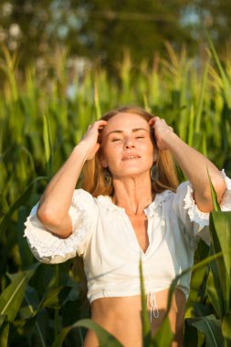 Yazın, batan güneşin ışığında, mısır tarlasında yeşil yaprakların arasında uzun kızıl saçlı güzel bir kadın..
