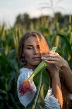 Yazın, batan güneşin ışığında, mısır tarlasında yeşil yaprakların arasında uzun kızıl saçlı güzel bir kadın..