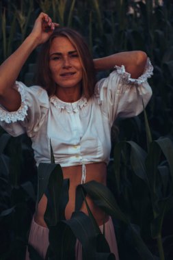 Yazın, batan güneşin ışığında, mısır tarlasında yeşil yaprakların arasında uzun kızıl saçlı güzel bir kadın..