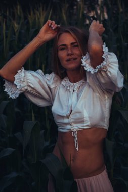 Yazın, batan güneşin ışığında, mısır tarlasında yeşil yaprakların arasında uzun kızıl saçlı güzel bir kadın..