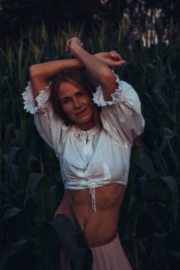 Yazın, batan güneşin ışığında, mısır tarlasında yeşil yaprakların arasında uzun kızıl saçlı güzel bir kadın..