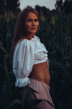 Yazın, batan güneşin ışığında, mısır tarlasında yeşil yaprakların arasında uzun kızıl saçlı güzel bir kadın..