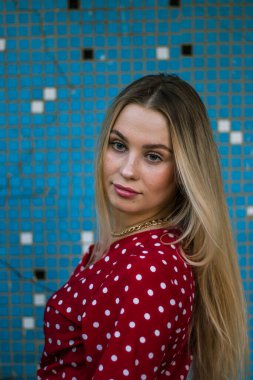 Çekici, güzel, Avrupalı bir kadın model. Mavi bir duvarın arka planında beyaz bir dairede kırmızı elbiseli güzel sarışın kadın. Doğal yumuşak akşam ışığı.