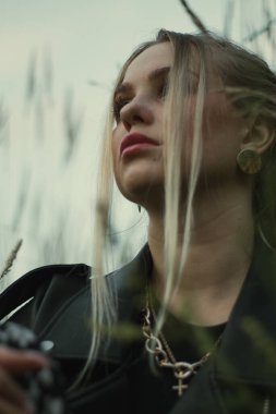 Mavi gözlü, genç, güzel bir sarışının portresi. Arka planda çimenlerin üzerinde yakın plan çekilmiş bir kadın. Doğal yumuşak akşam ışığı