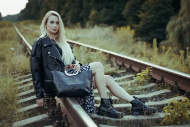 Siyah elbiseli güzel bir kız, tren raylarında. Güzel sarışının keyfi yerinde. Güzel, yumuşak akşam ışığı