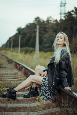 Siyah elbiseli güzel bir kız, tren raylarında. Güzel sarışının keyfi yerinde. Güzel, yumuşak akşam ışığı