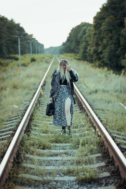 Siyah elbiseli güzel bir kız, tren raylarında. Güzel sarışının keyfi yerinde. Güzel, yumuşak akşam ışığı