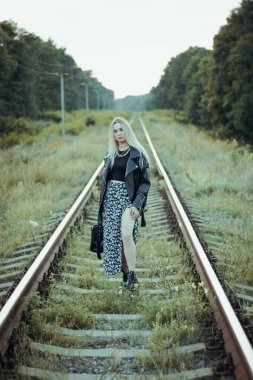 Siyah elbiseli güzel bir kız, tren raylarında. Güzel sarışının keyfi yerinde. Güzel, yumuşak akşam ışığı