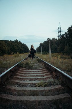 Siyah elbiseli güzel bir kız, tren raylarında. Güzel sarışının keyfi yerinde. Güzel, yumuşak akşam ışığı