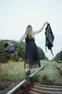 Siyah elbiseli güzel bir kız, tren raylarında. Güzel sarışının keyfi yerinde. Güzel, yumuşak akşam ışığı