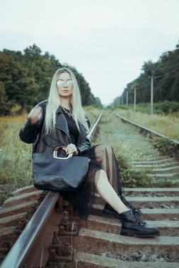 Siyah elbiseli güzel bir kız, tren raylarında. Güzel sarışının keyfi yerinde. Güzel, yumuşak akşam ışığı