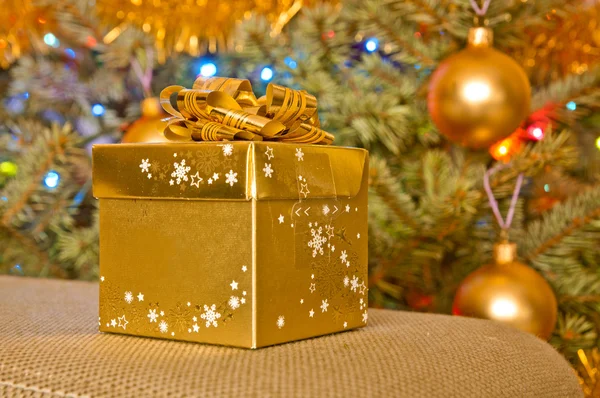 Golden Christmas gift next to a christmas tree — Stock Photo, Image