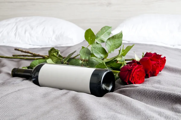 Garrafa de vinho e rosas na cama - conjunto romântico — Fotografia de Stock