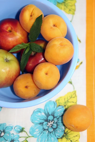 Apricots and apples in blue plastic bowl on napkin. — Stock Photo, Image