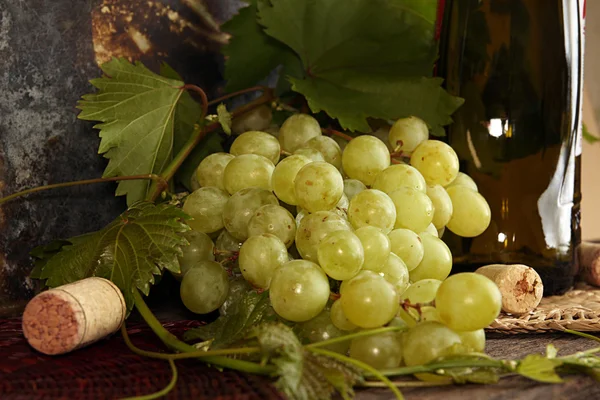 Grappolo verde uva con foglie contro bottiglia di vino di sfondo — Foto Stock