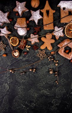 Dekorlu zencefilli kurabiye, portakallı meyve dilimleri, siyah beton arka planda Noel ve yeni yıl süsü olan tebrik kartı. Yılbaşı tatili geçmişinin genel gideri. Üst Manzara. Boşluğu kopyala