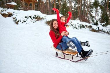 Anne ve kızı ormanda karda kızakla.